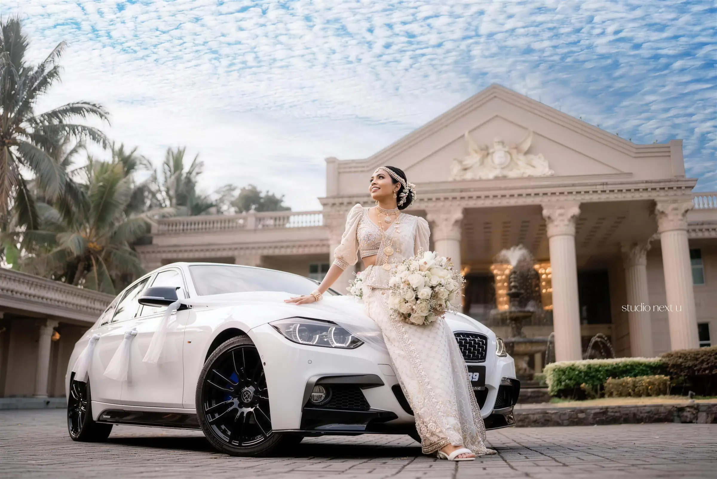 A bride in a Kandyan saree beside her wedding car in Grand Mondo's arrival court