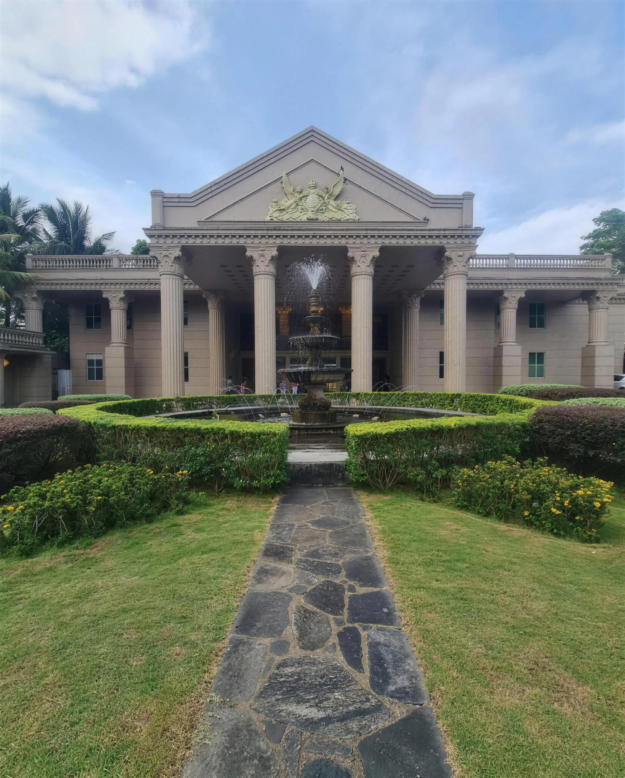A stone path across manicured lawns to Grand Mondo's portico and fountain